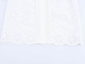 Detail of white cotton blouse with floral Broderie Anglaise embroidery and pleated hem