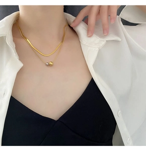 Detail of layered titanium steel necklace with gold and silver bead pendants on model