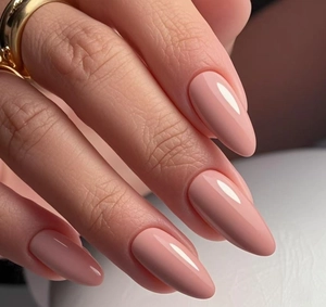 Gros plan d'ongles amandes rose nude brillants avec une bague minimaliste dorée