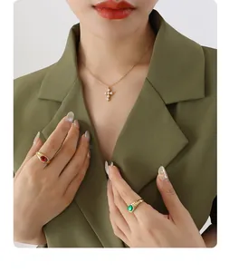 Detail of pearl cross pendant and gemstone rings worn with an olive green blazer