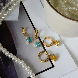 Flat lay of 18K gold plated hoop earrings featuring square blue and yellow zircon charms
