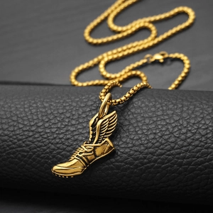 Pendentif baskets dorées avec ailes sur chaîne tressée posé sur un support en cuir noir