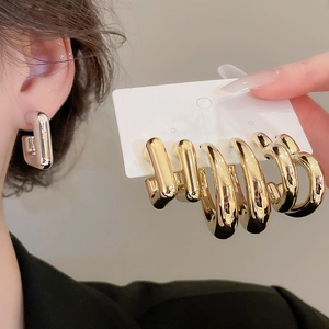 Gros plan de boucles d'oreilles carrées argentées et créoles dorées sur un présentoir