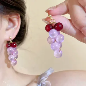 Détail de boucles d'oreilles perles en forme de raisin violet portées sur l'oreille