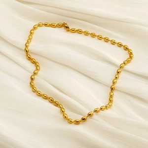 Fashionable gold stainless steel rice bead necklace on elegant cream silk background