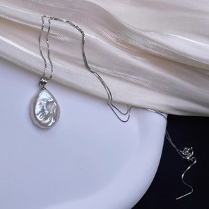 Close-up of a Baroque freshwater pearl pendant on a silver box chain over a ceramic plate
