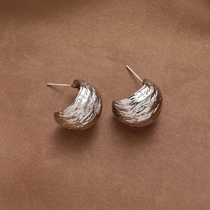 Detail of silver C-shape earrings with unique hammered texture on silk fabric