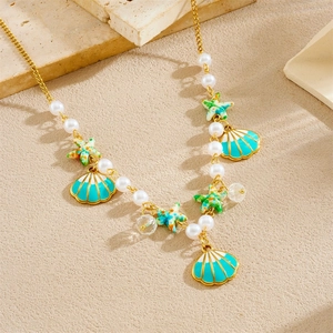 Golden necklace with green starfish and blue shell pendants on a textured sand background