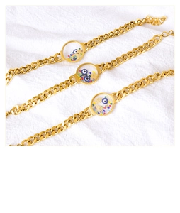 Detail of gold chain bracelets featuring evil eye charms and colorful sequins on fabric