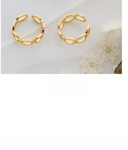 Détail d'une bague dorée à maillons ovales sur tissu texturé blanc avec fleurs séchées
