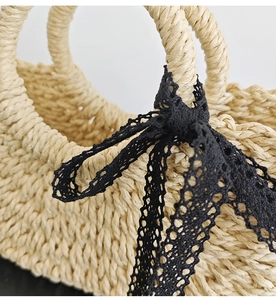 Close-up of beige woven straw tote bag featuring detailed black lace bow decoration