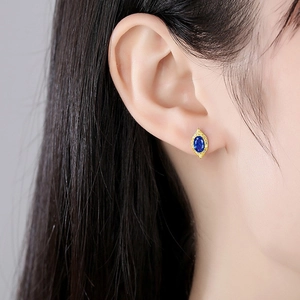Close-up of gold stud earring featuring a dark blue oval gemstone with diamond halo