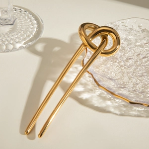 Detail of a golden U-shaped hair pin with a unique rope knot design in a polished finish