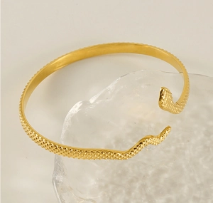 Detailed shot of 18k gold snake skin texture cuff bracelet on a textured glass prop
