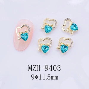 Détail macro d'un bijou d'ongle coeur doré avec texte Love et strass bleu-vert