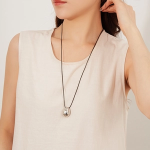 Pendentif ovale argenté minimaliste sur cordon de cire noir porté par un mannequin