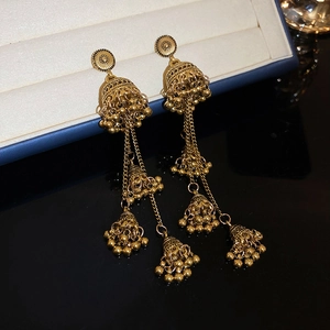 Detail of vintage golden Jhumka earrings with hollow bell shapes and chain tassels