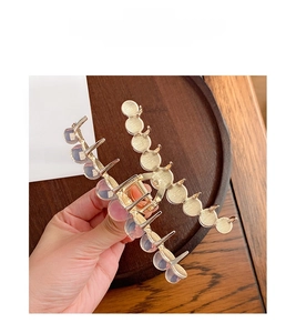 Detail view of a large gold metal shark clip featuring iridescent beads on wood