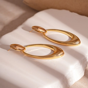 Detailed close-up of golden geometric oval drop earrings on a white textured stone base