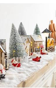 Close-up of lighted wooden house and miniature pine trees in a snowy Christmas scene