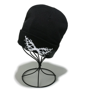 Detail of black knitted beanie with white pixelated butterfly jacquard on metal stand