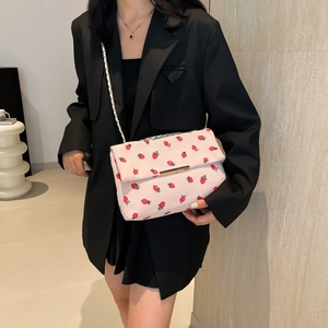 Detailed close-up of pink strawberry print shoulder bag with gold chain strap on black blazer