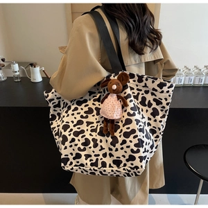 Detail of large canvas cow print tote bag with a cute mouse plush charm on shoulder