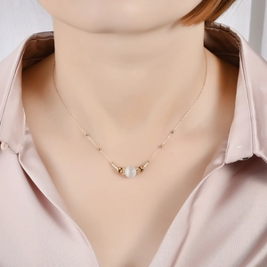 Close-up of a delicate gold stainless steel necklace with a translucent white bead on a model