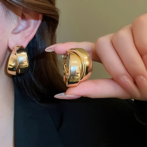 Macro detail of wide gold hoop earrings featuring a polished mirror-like metallic finish