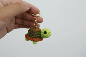 Dettaglio di portachiavi a forma di tartaruga lavorato a maglia tenuto in una mano