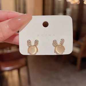 Close-up of gold rabbit stud earrings with sparkling crystals and round cat eye stone
