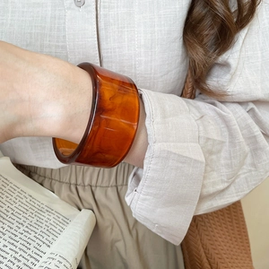 Detail of a wide amber resin bangle featuring marble textures paired with a linen shirt