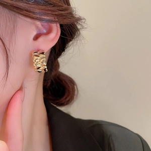 Close-up of golden geometric earrings with irregular textured finish on model's ear
