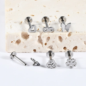 Detailed macro view of silver stainless steel lip studs with heart, butterfly and clover motifs