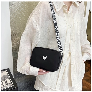Detail of nylon crossbody bag featuring a butterfly badge and lettered wide shoulder strap
