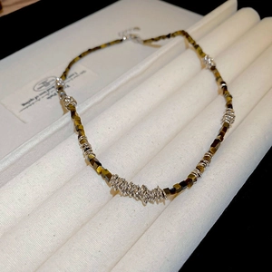 Macro detail of tiger eye stone necklace with gold-plated clasp on a white velvet tray