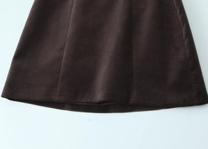 Vue détaillée de l'ourlet d'une robe en velours marron avec coutures sur fond blanc