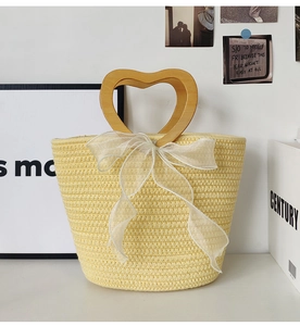 Detail of heart-shaped wooden handle on a yellow straw handbag with white ribbon bow