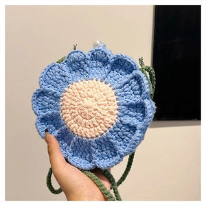 Detail of crochet flower bag featuring blue petals, beige center and white pearl accent