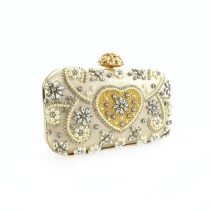 Macro shot of handmade champagne gold evening clutch with pearls and crystal heart pattern