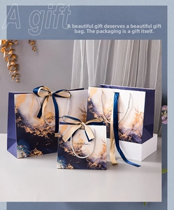 Three sizes of marble patterned gift bags with blue and gold ribbons on white surface