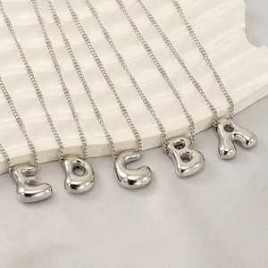 Close-up of silver bubble letter necklaces A-E on a minimalist white wavy display
