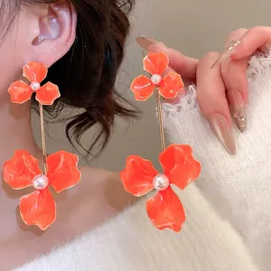Elegant long orange flower earrings with pearls and gold rods shown on female model
