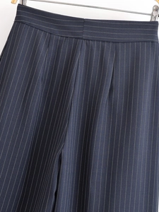 Détail du pantalon à rayures verticales montrant la taille haute plissée et les coutures