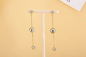 Detailed view of long gold tassel earrings with sparkling round rhinestones on a T-stand
