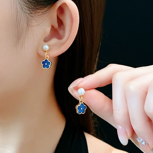 Close-up of golden earrings with white pearls and blue four-leaf clover pendants