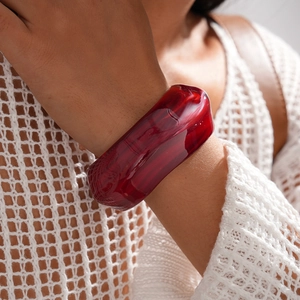 Close-up of a wide translucent deep red acrylic geometric bangle on a white crochet fabric