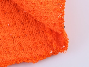 Makroaufnahme von orangefarbenem Strickstoff mit feinen Pailletten und Texturdetails