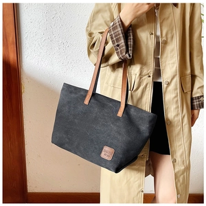 Detail of black canvas tote bag with brown faux leather label and shoulder straps