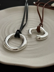 Close-up of polished silver circle pendant and C-shaped ring on long leather cords